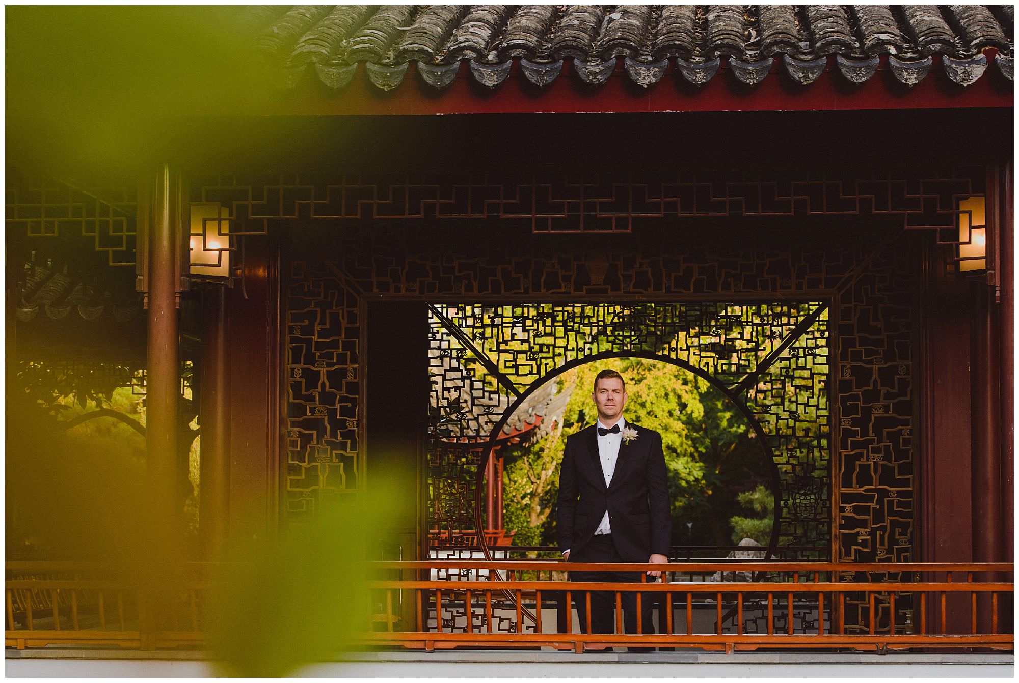 Groom in classic black tie suit stands in Dr. Sun Yat-Sen Classical Chinese Gardens at sunset after his intimate wedding, Vancouver wedding photographer